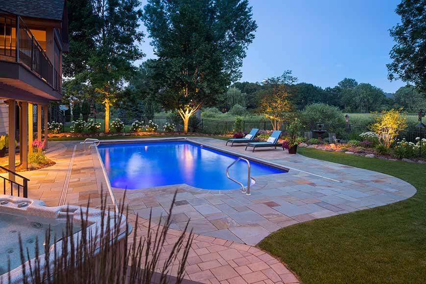 Illuminated backyard pool and garden at twilight.