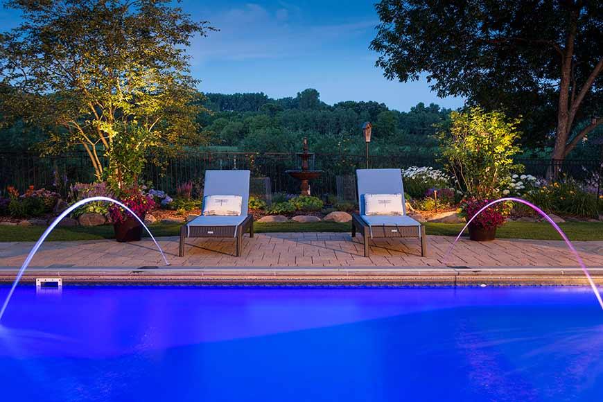 Nighttime view of illuminated pool and lounge chairs.