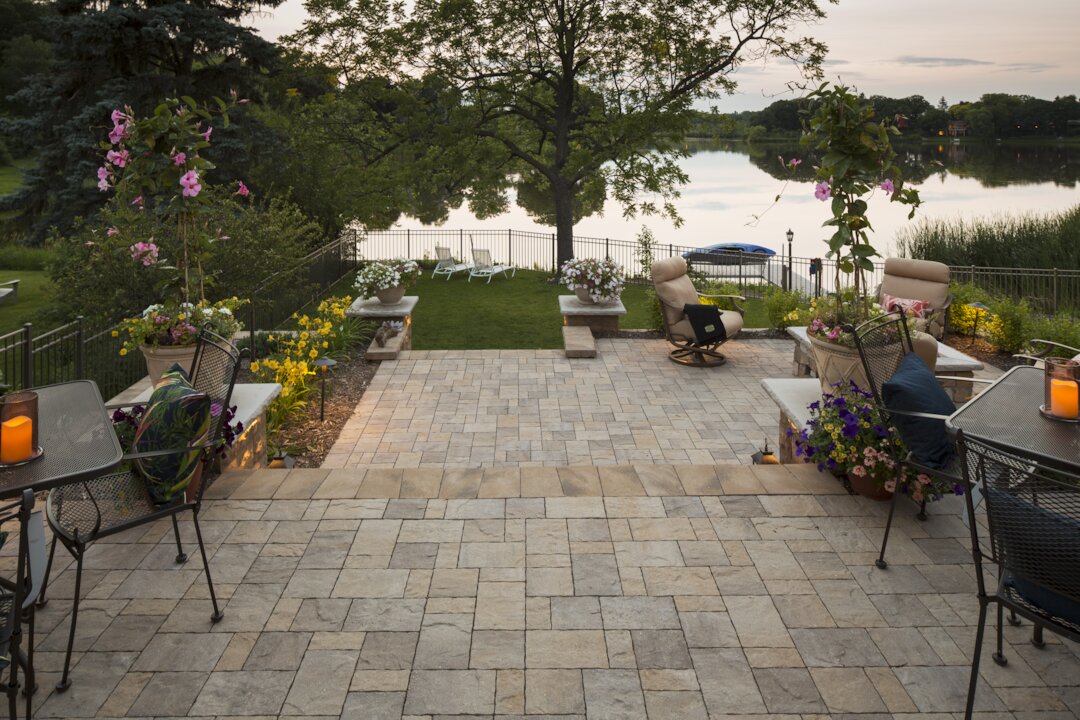 Elegant lakeside patio with blooming flowers and chairs.
