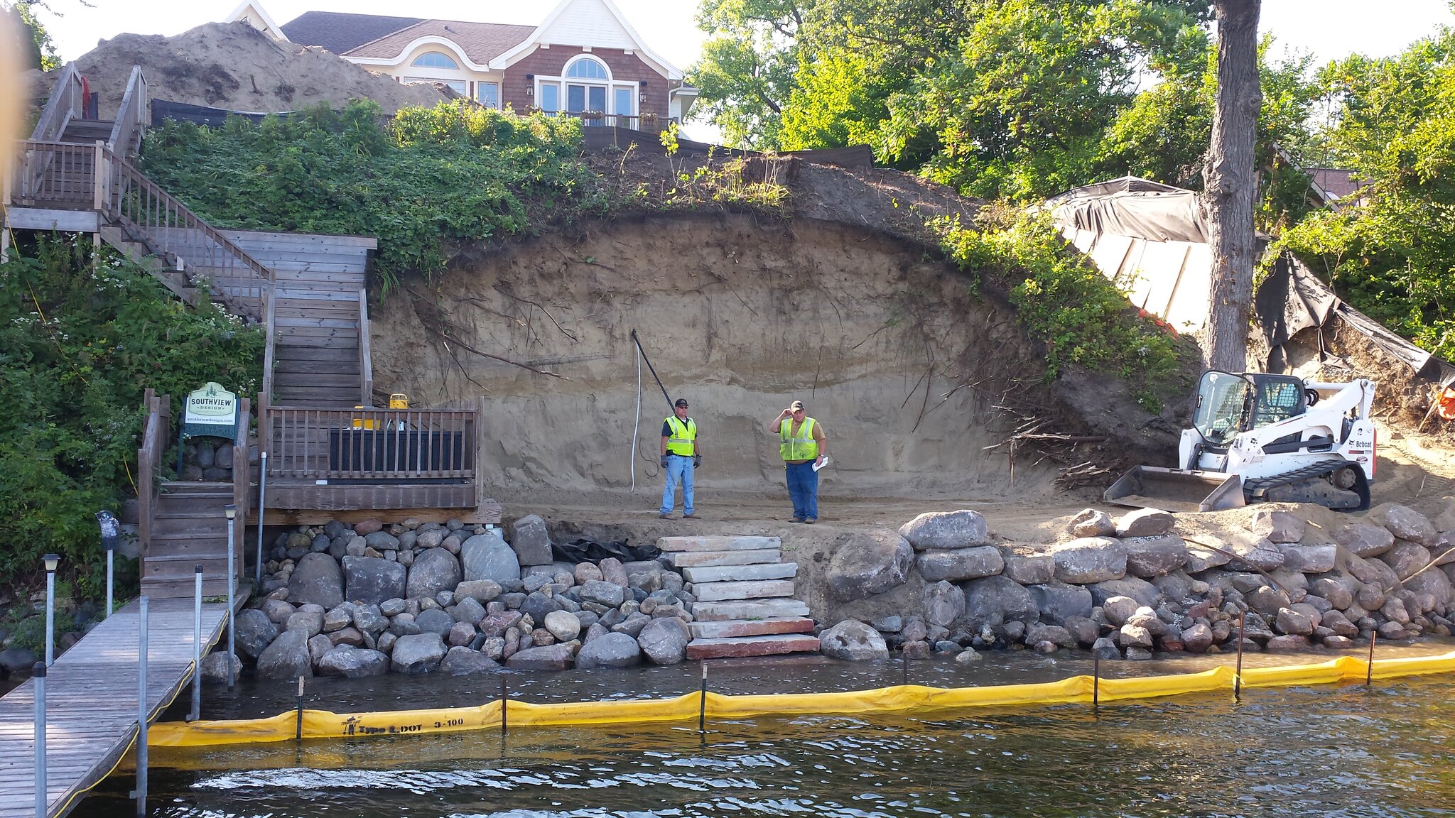 Construction workers excavate lakeside hillside site.