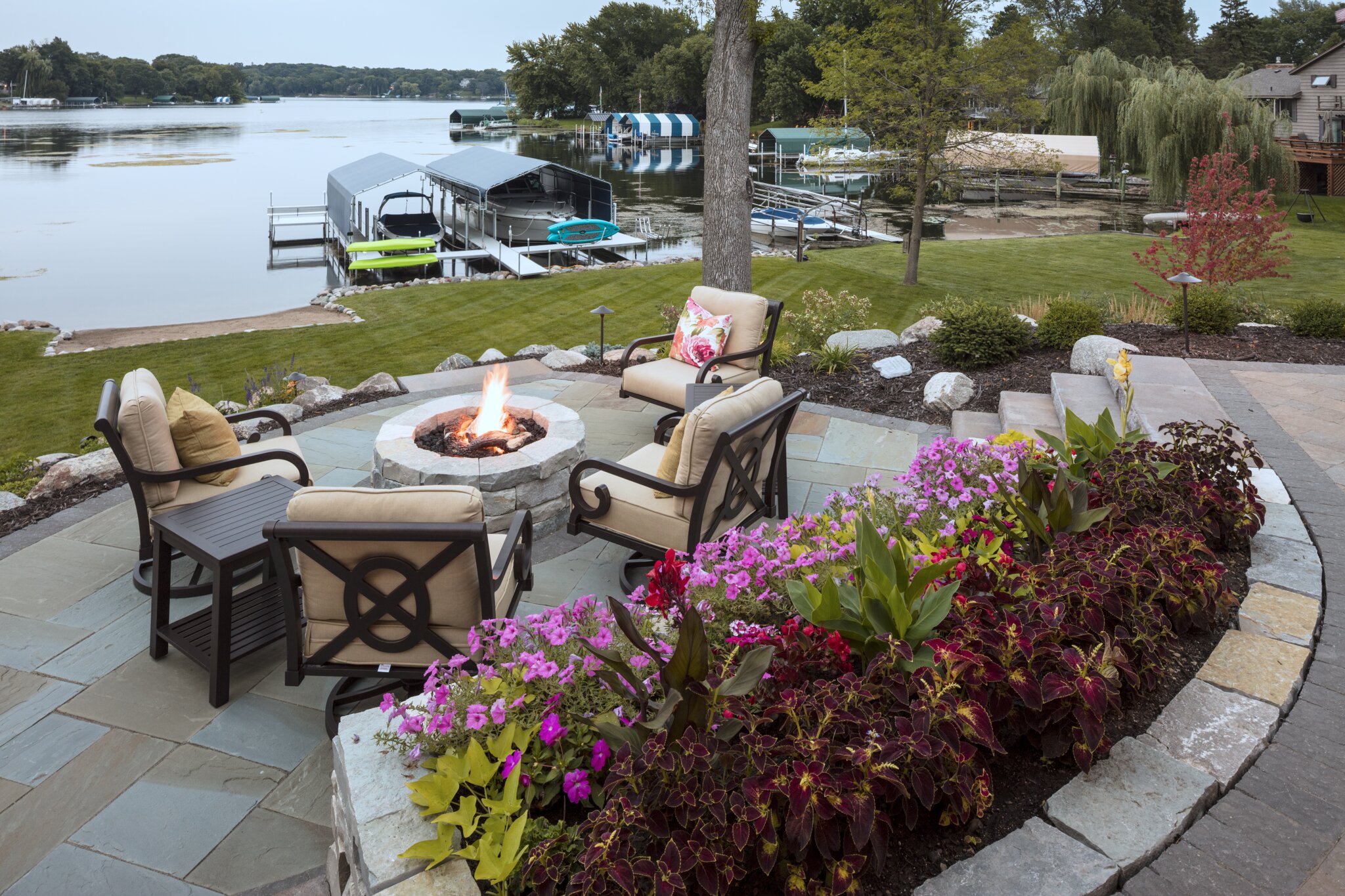 Lakeside patio with fire pit and garden view.