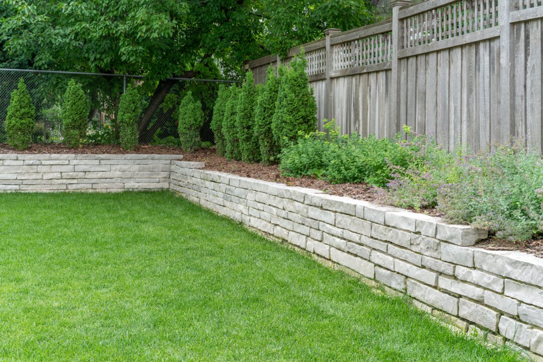 Stone retaining wall with green lawn and trees.