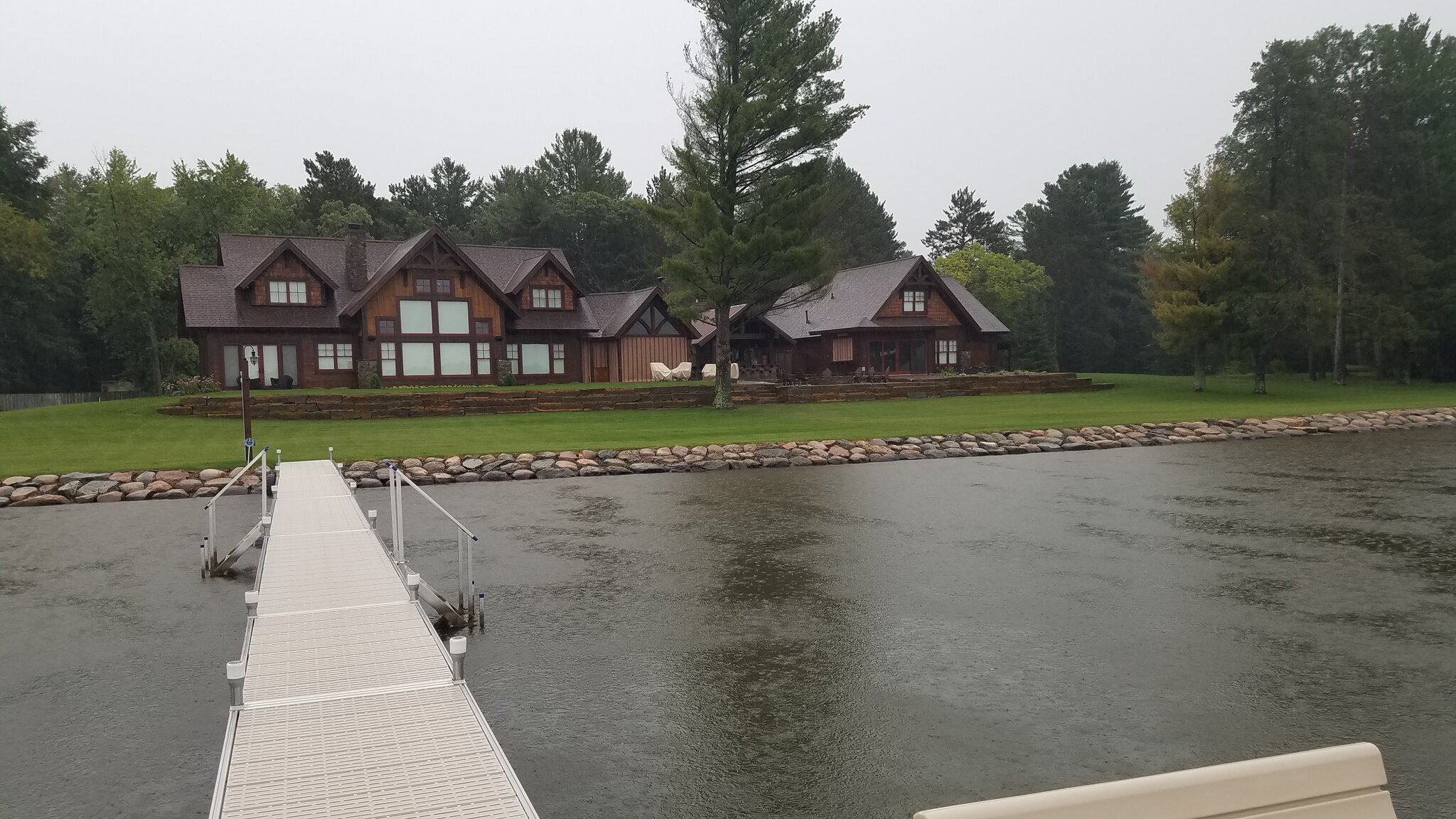 Wooden house by lake with dock, surrounded by trees.