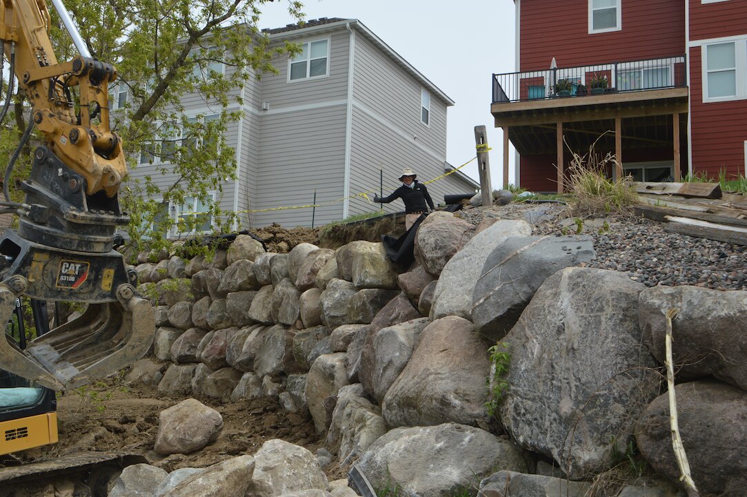 Excavator building stone retaining wall near houses.