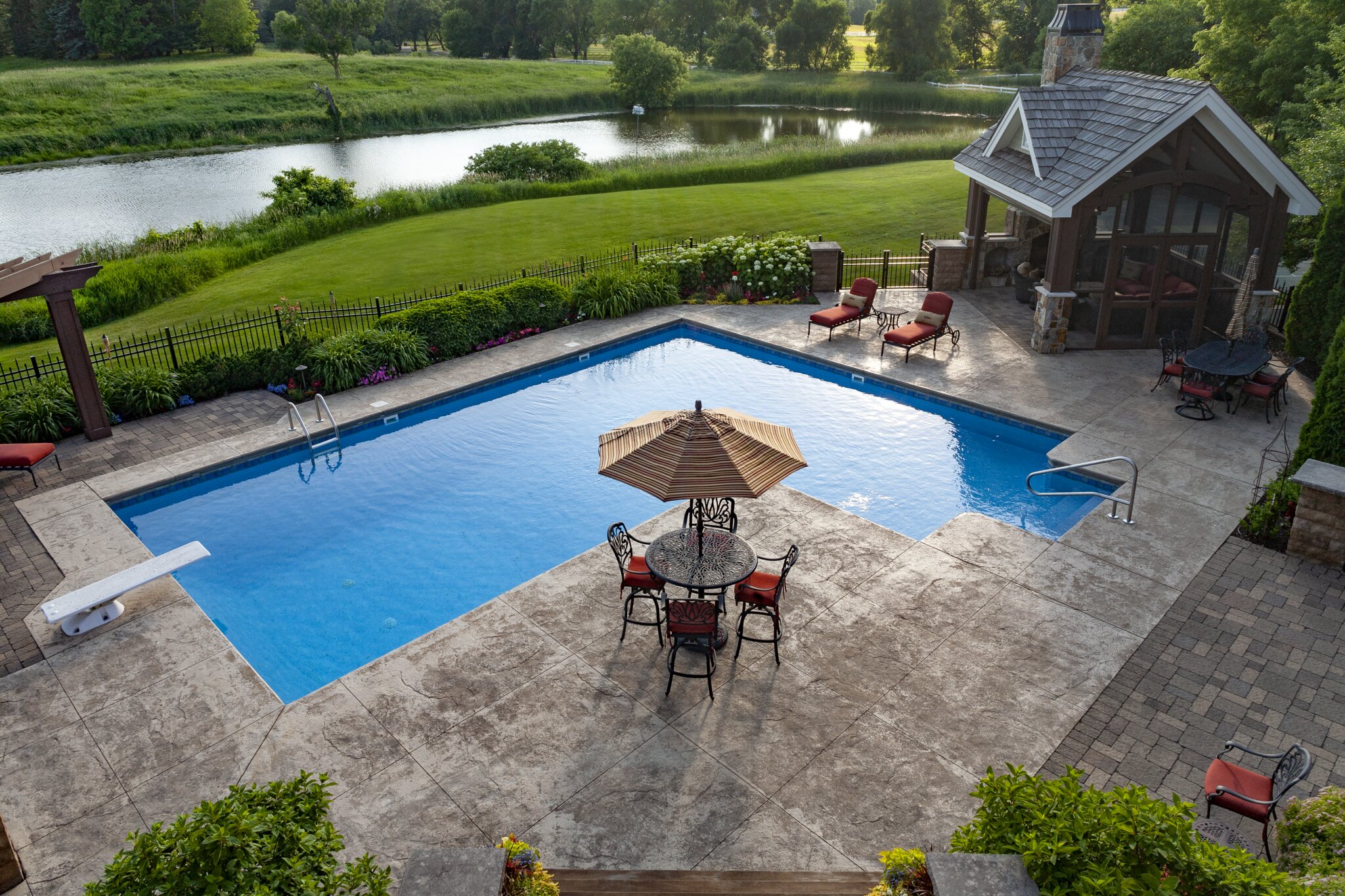 Backyard pool with patio and gazebo by a lake.