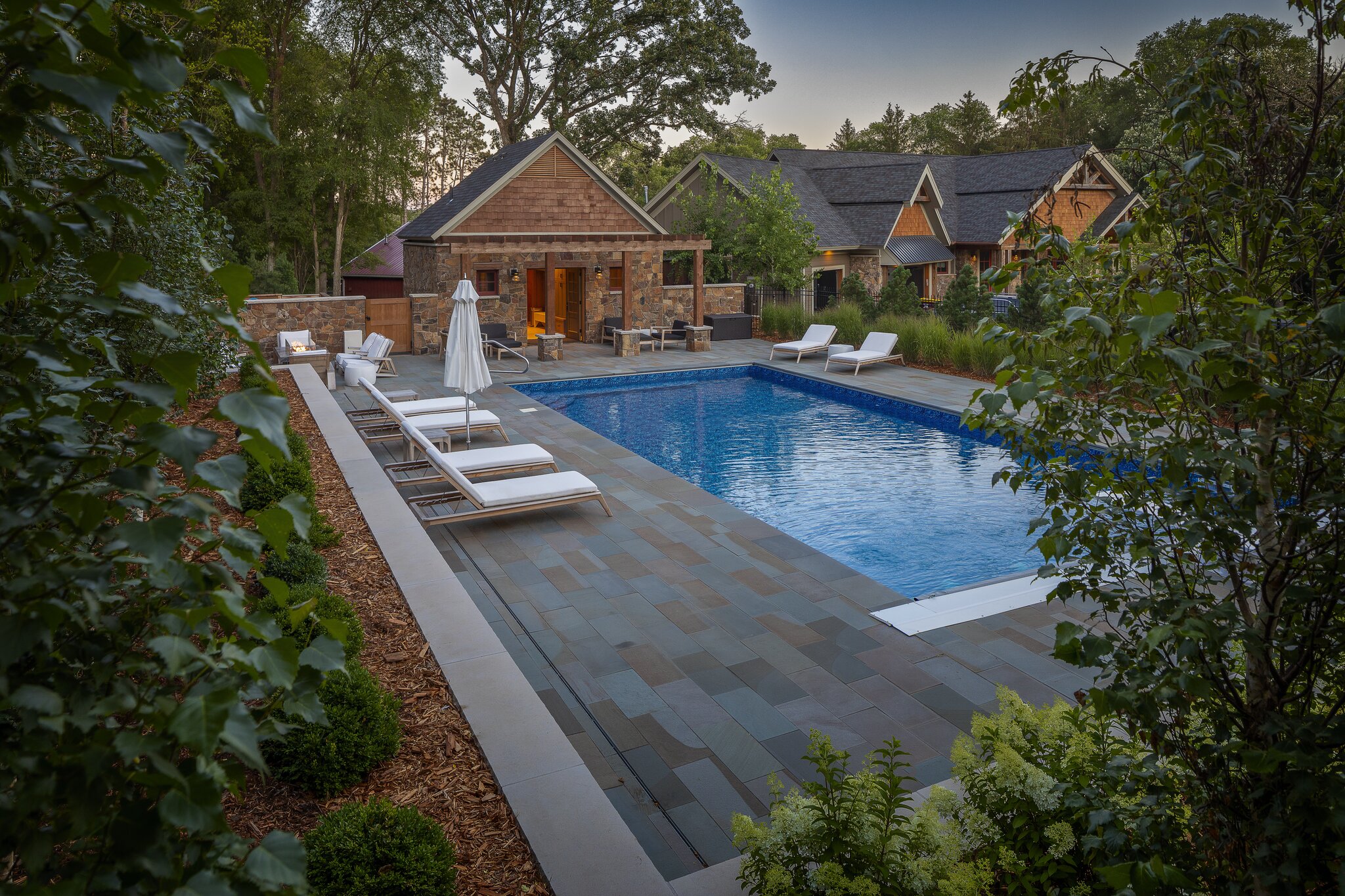 Luxury backyard pool with lounge chairs and greenery.