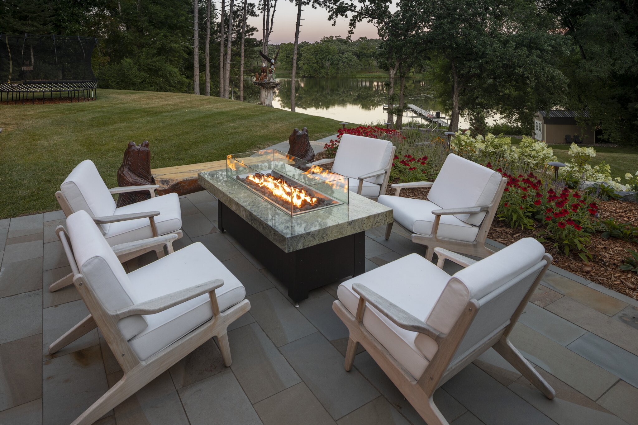 Outdoor patio with fire pit and chairs near lake.