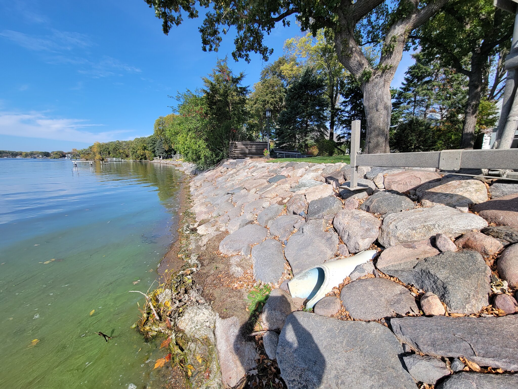 Lakeshore with rock retaining wall and drain pipe.