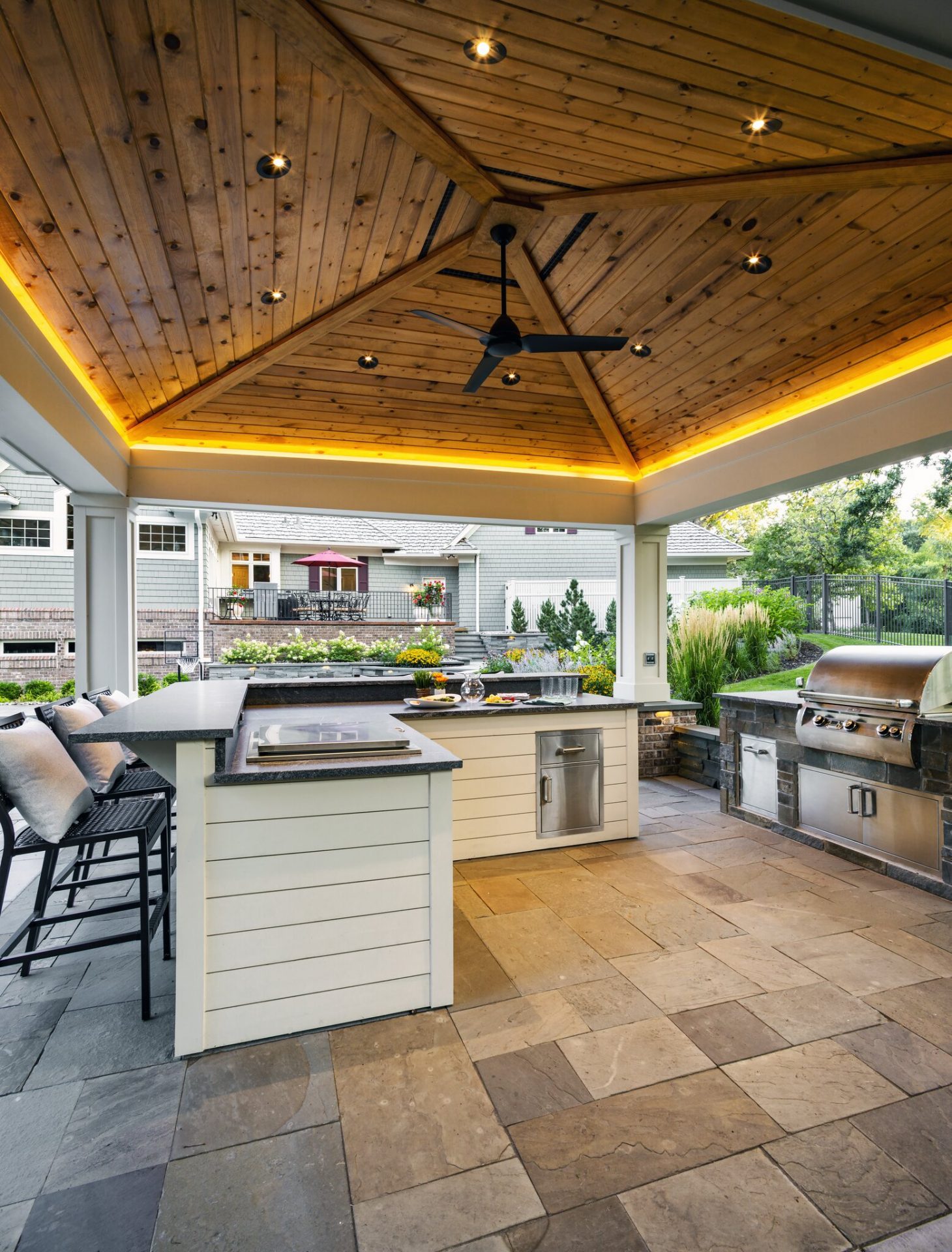 Modern outdoor kitchen with wooden ceiling and grill.
