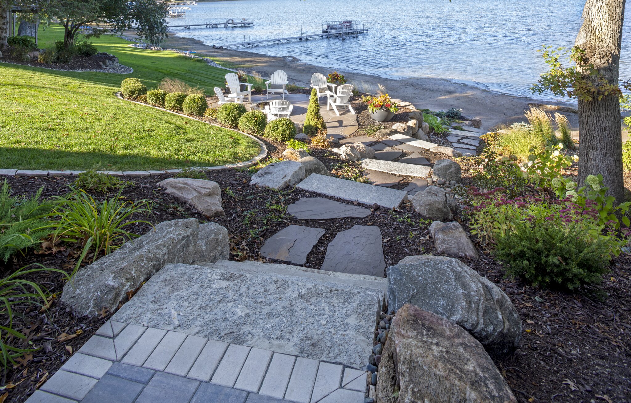 Lakeside patio with Adirondack chairs and stone path.
