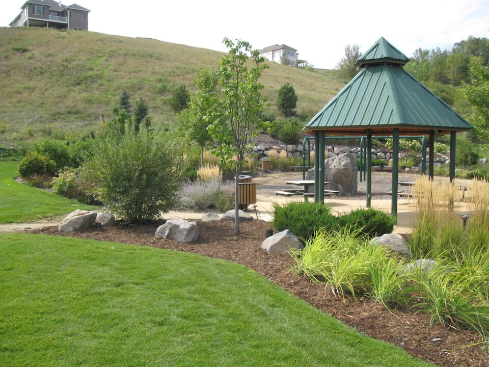 Park with pavilion, trees, and grassy hill.