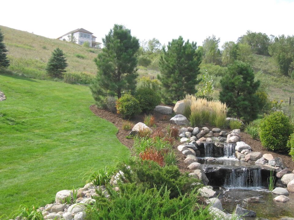 Landscape with waterfall, trees, and house on hill.