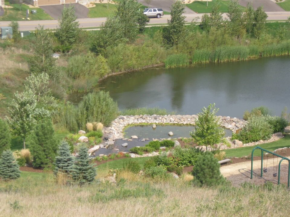 Landscape with pond, trees, playground, and road.