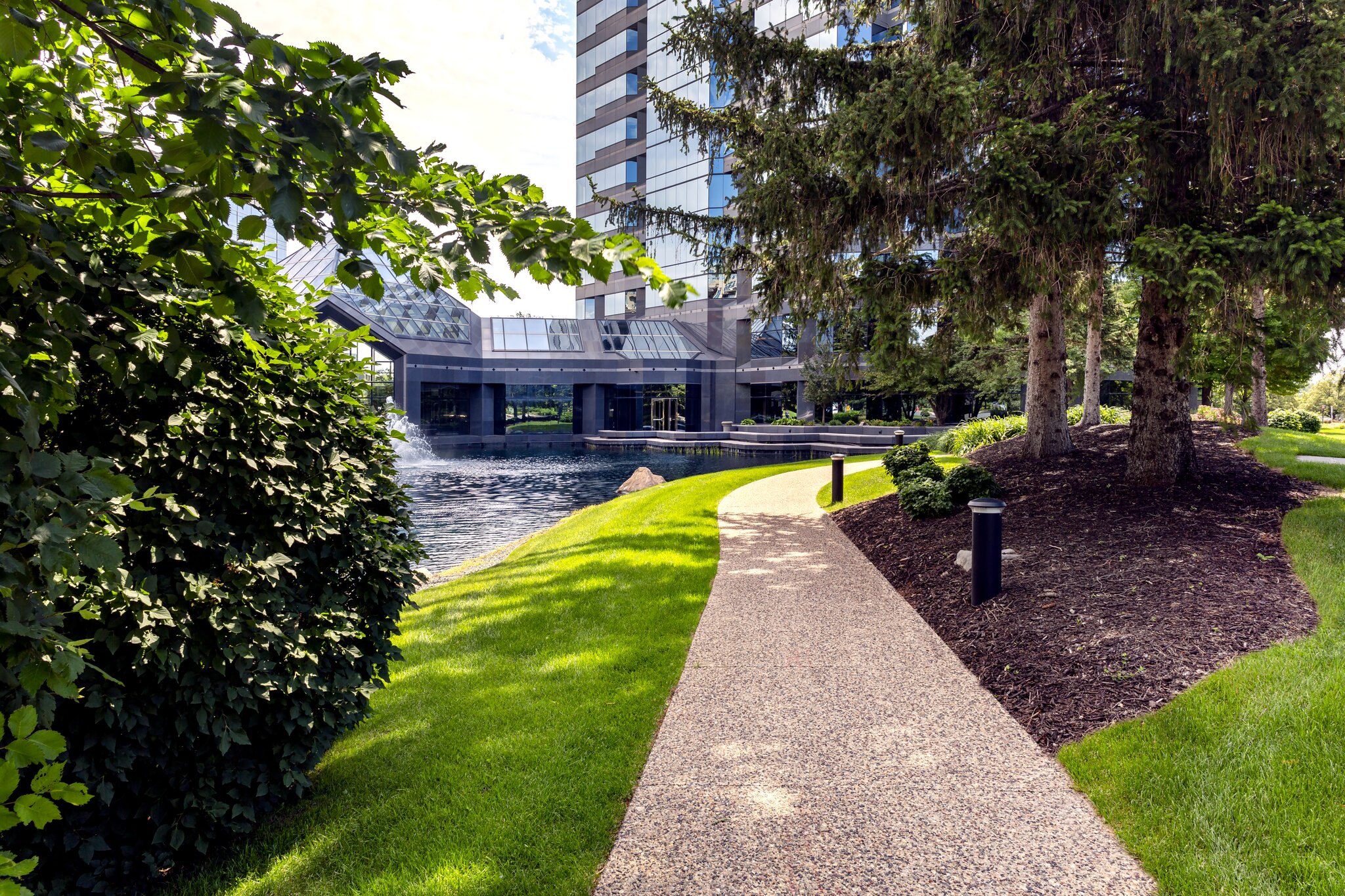 Scenic pathway by modern glass building and pond.