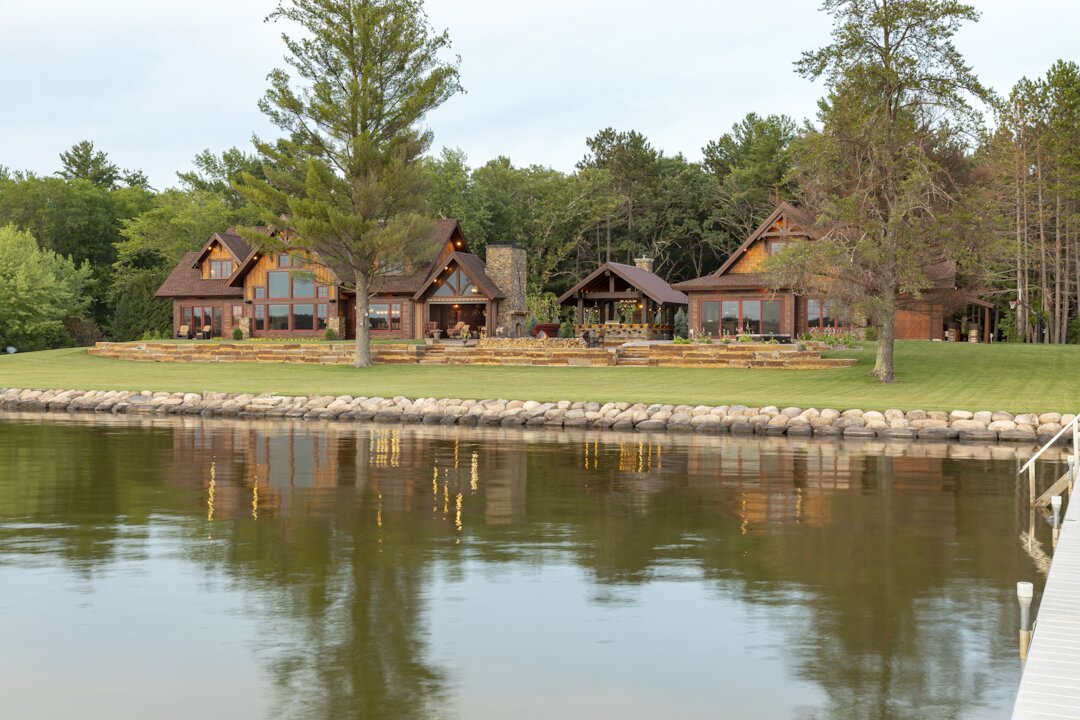 Large rustic house by a lake, surrounded by trees.