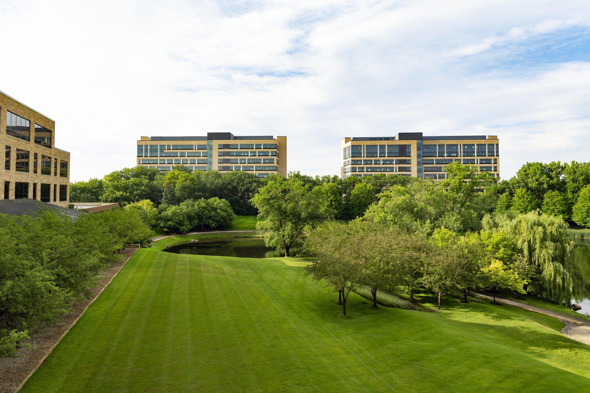 Modern buildings overlooking lush green park with pond.
