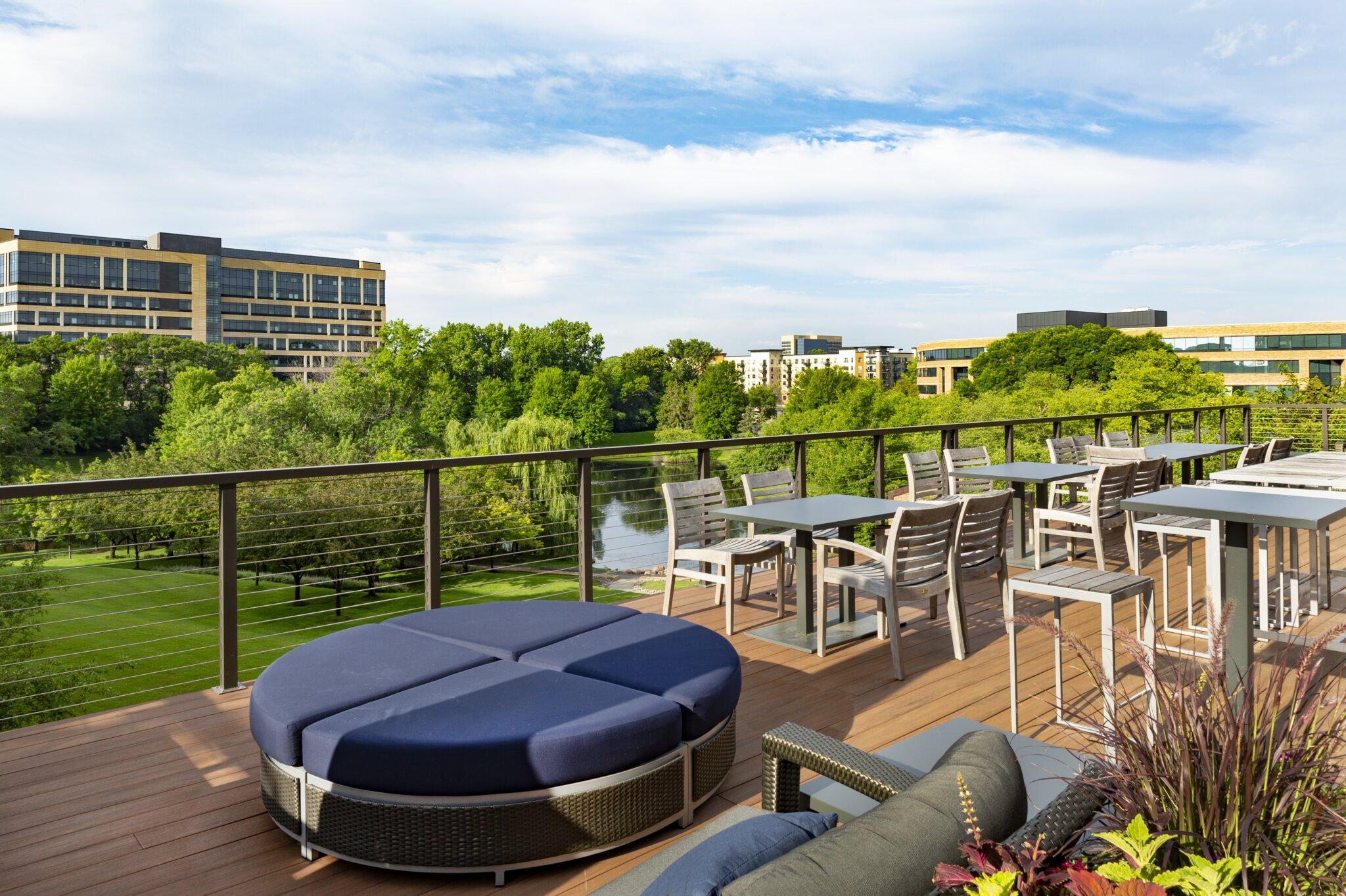 Rooftop deck with chairs, tables, and greenery view.