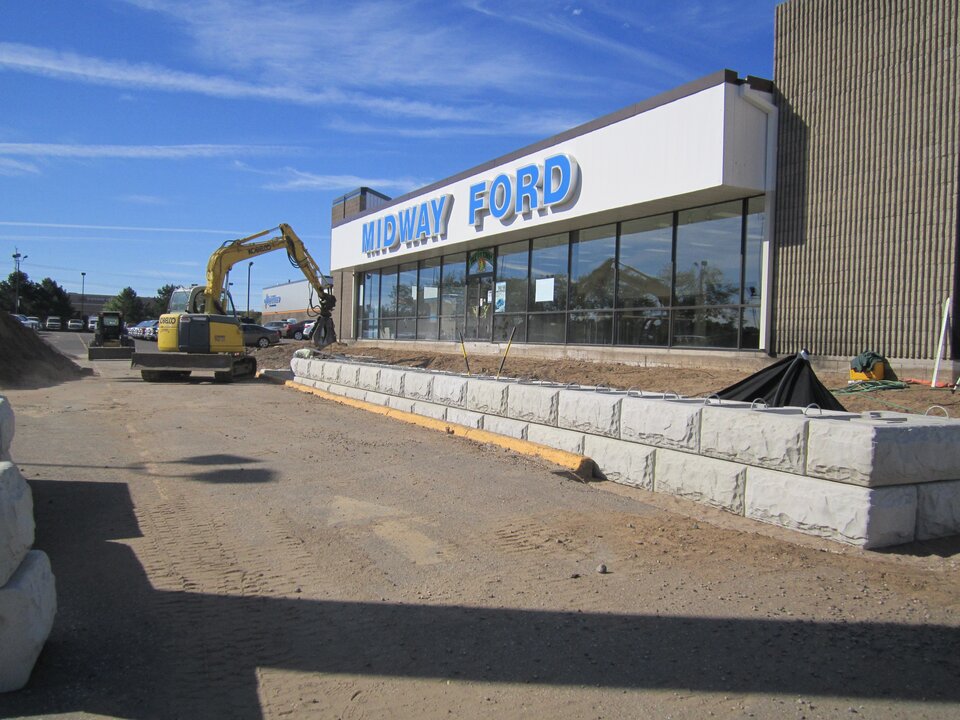 Construction site at car dealership under blue sky.