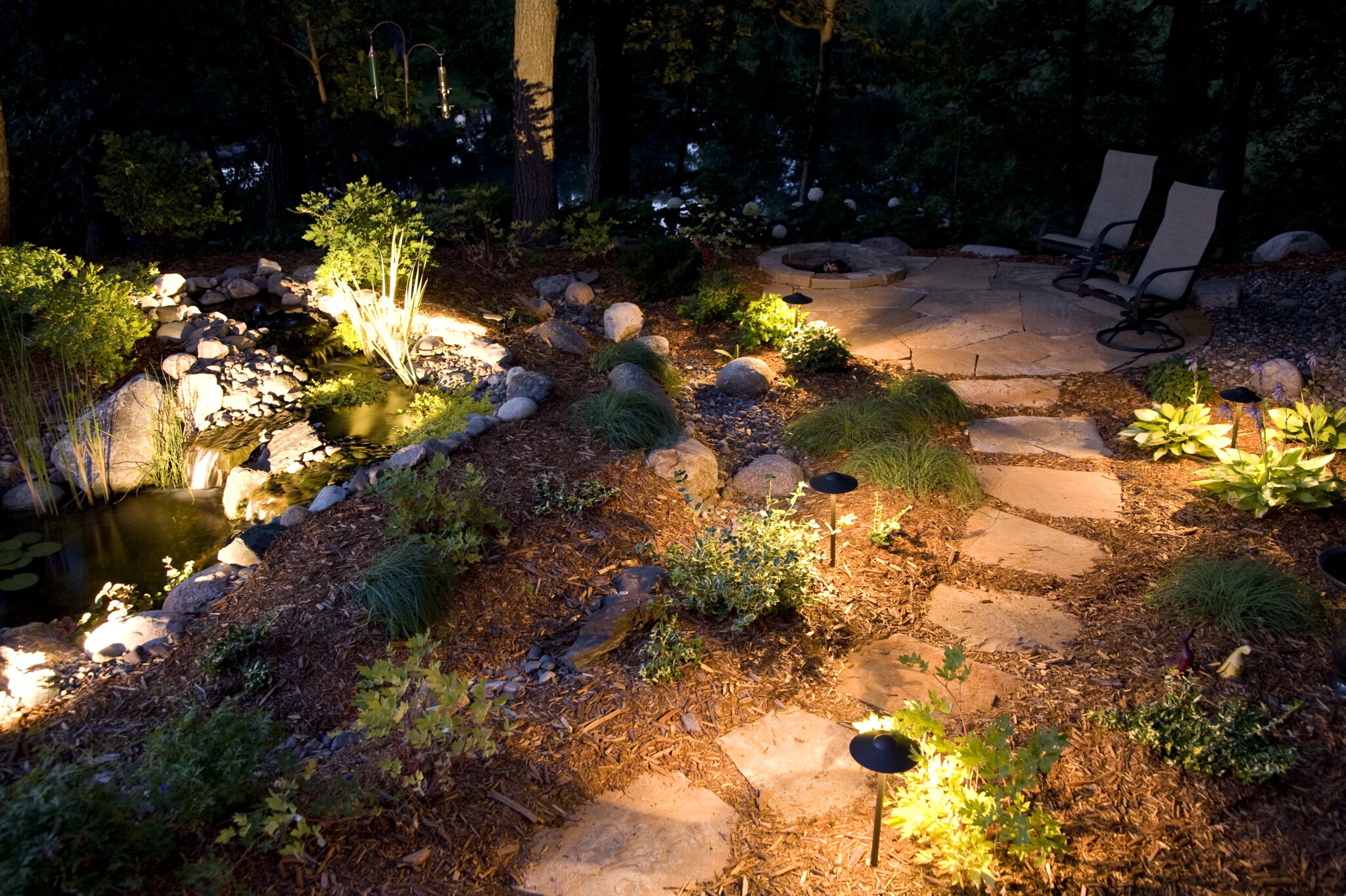 Illuminated garden path with stone steps and chairs.