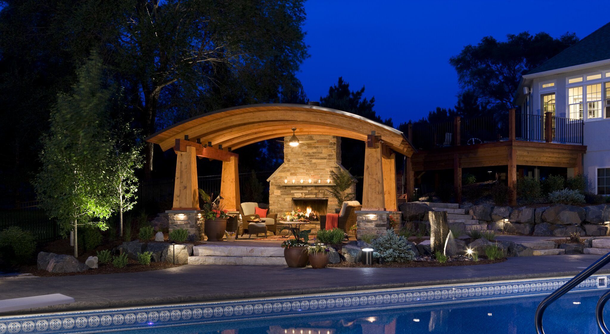 Cozy outdoor fireplace by illuminated pool at night.