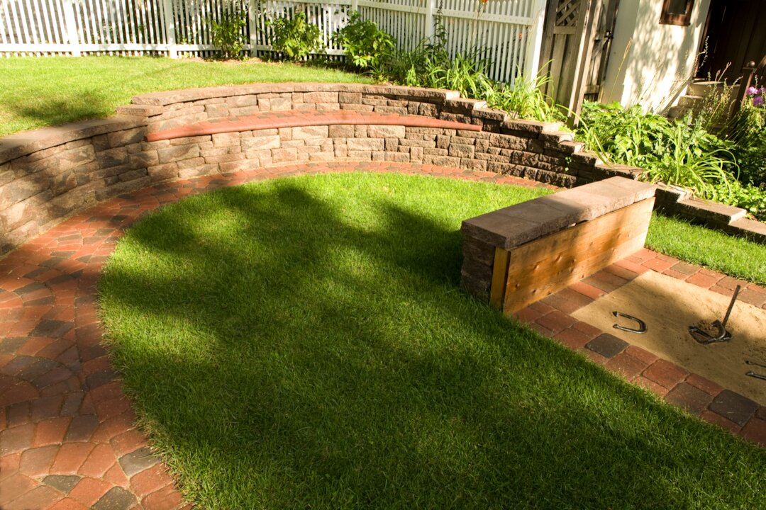 Backyard with grass, stone seating, and horseshoe pit.