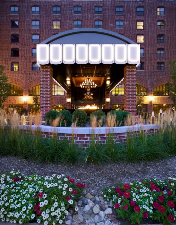 Brick building entrance with chandelier and flower garden.