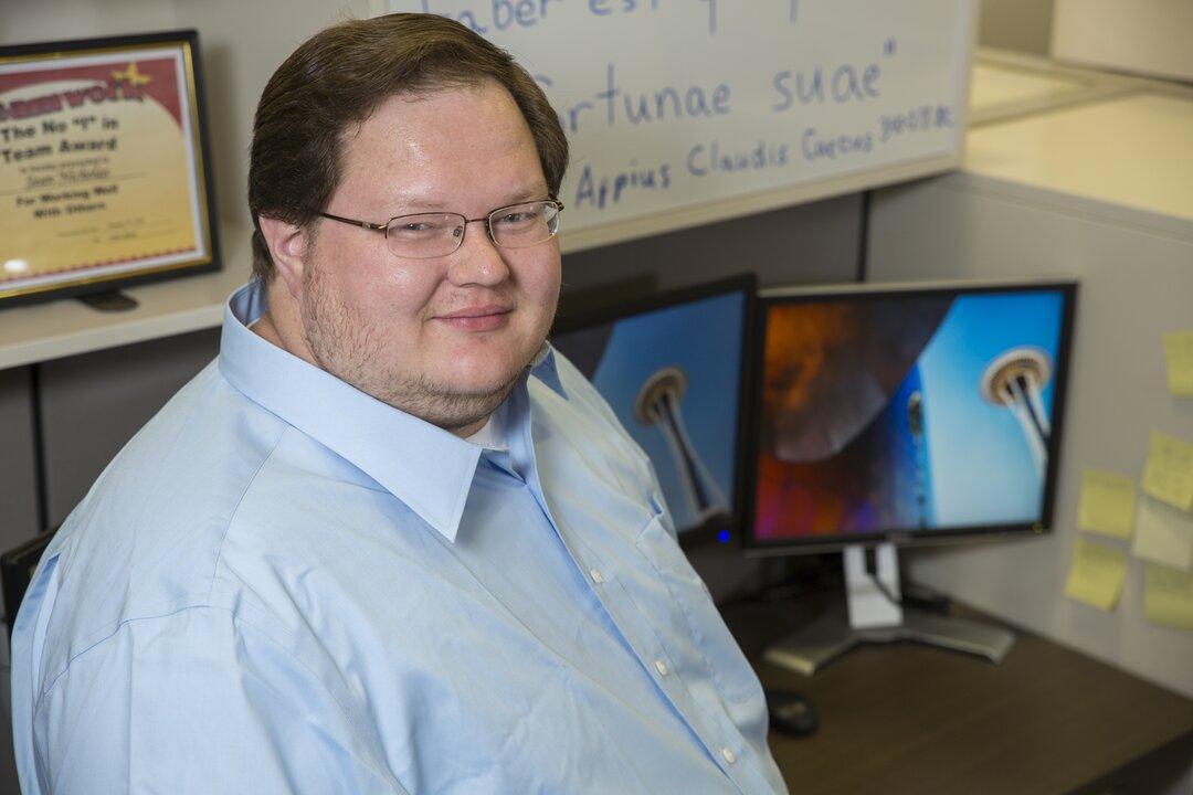 Smiling office worker at desk with computers