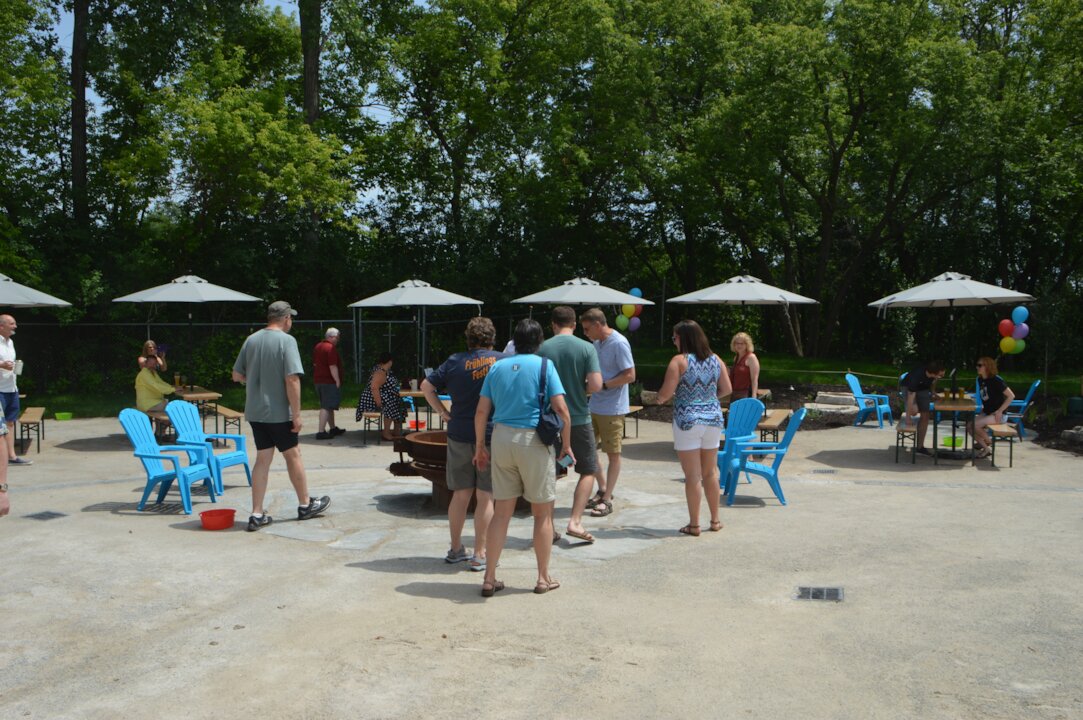 Outdoor gathering with people, chairs, and umbrellas.