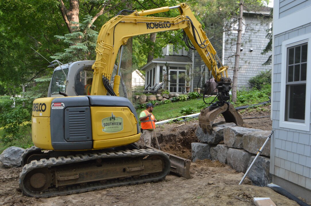 Excavator placing rocks in residential construction site.