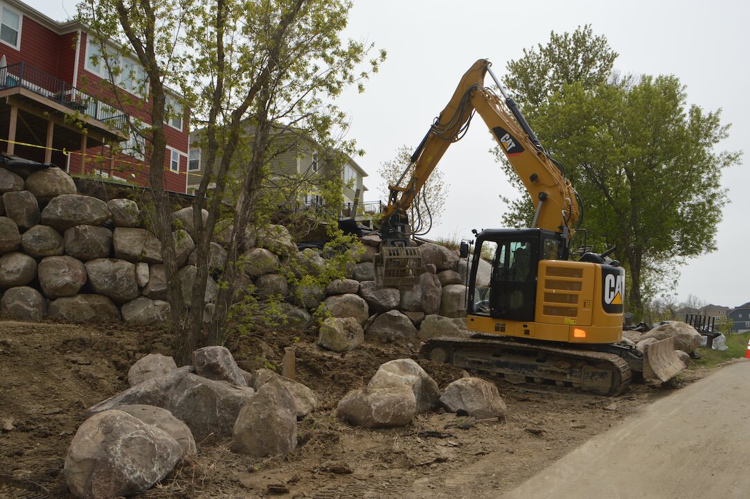 Excavator moving rocks near residential area.