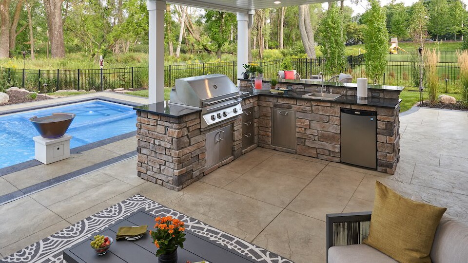 Outdoor kitchen patio with grill near swimming pool.