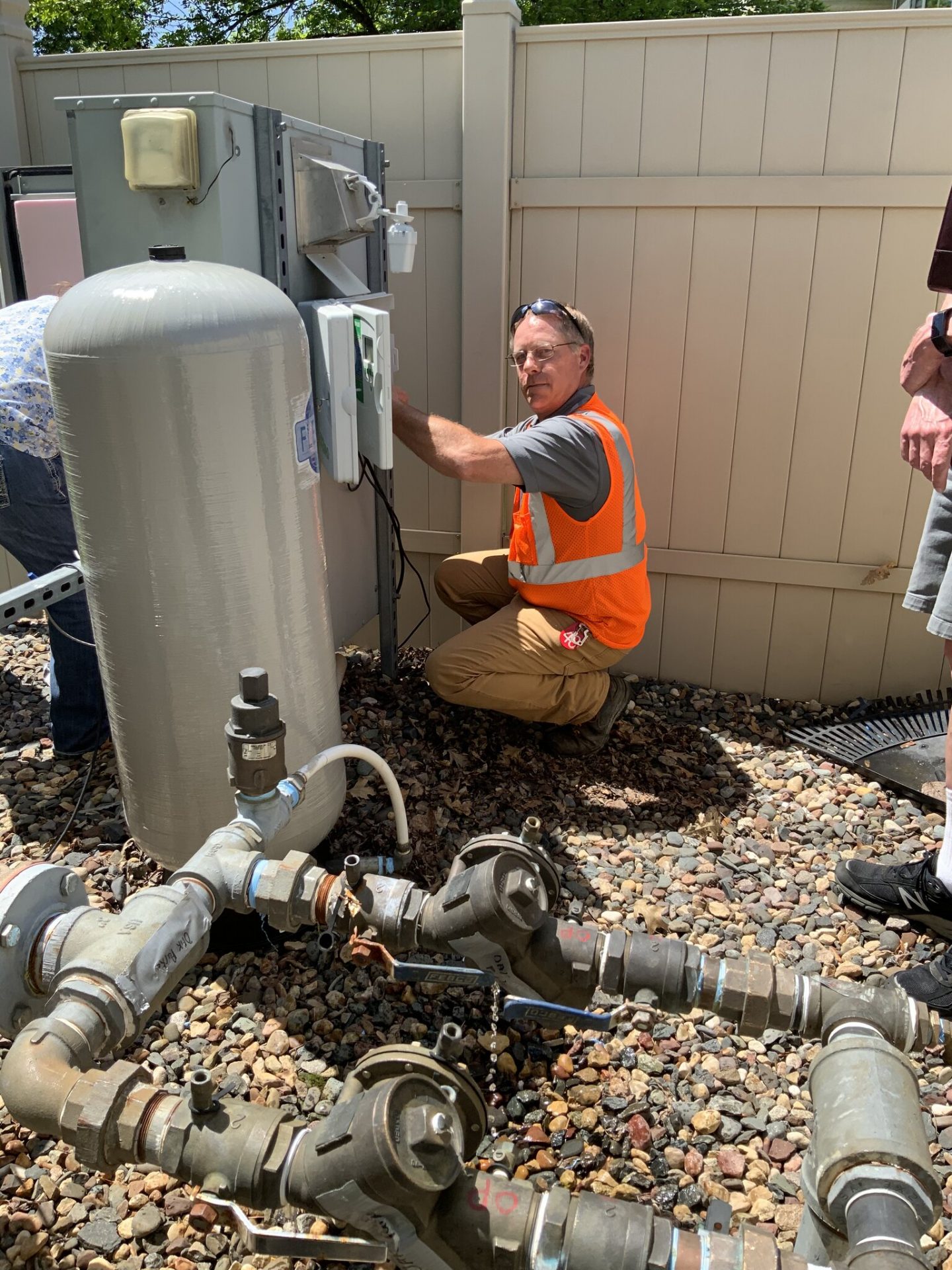Worker inspecting outdoor plumbing system with tools.