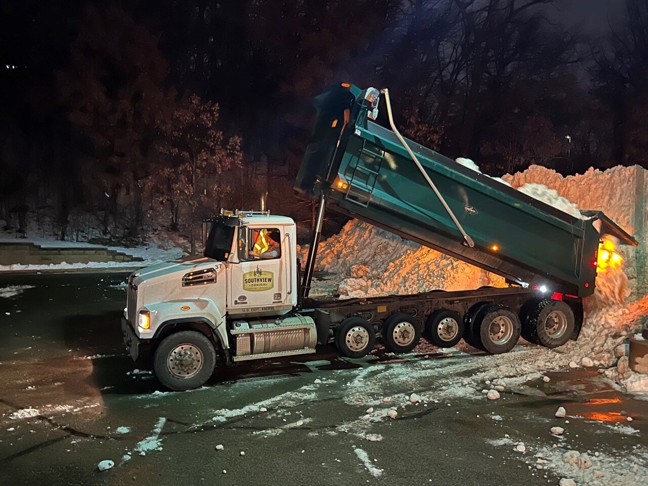 Dump truck unloading snow in a parking lot.