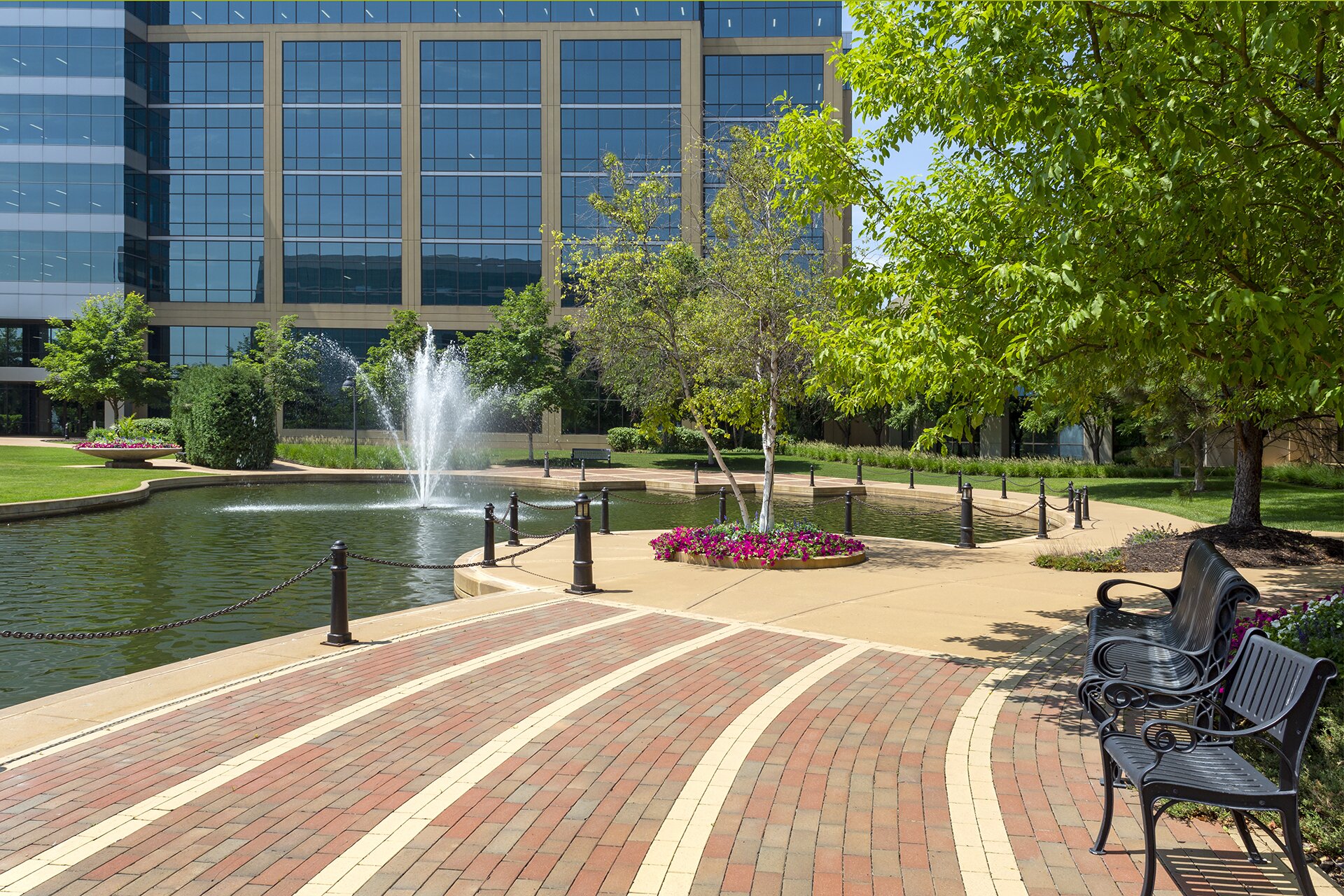 Office building with fountain and benches in park.