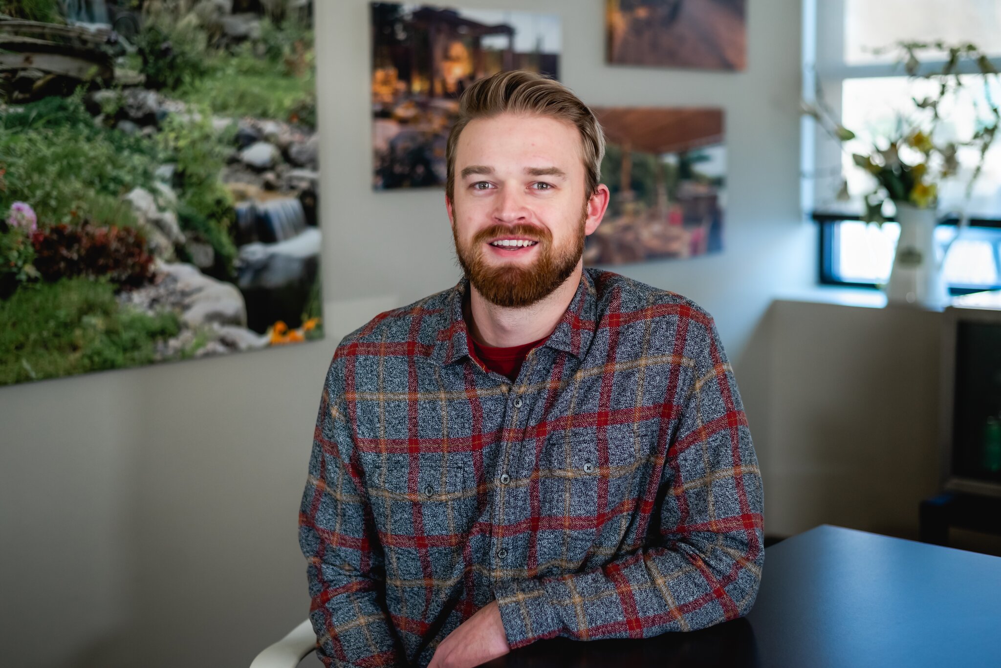 Man in plaid shirt sitting indoors, smiling