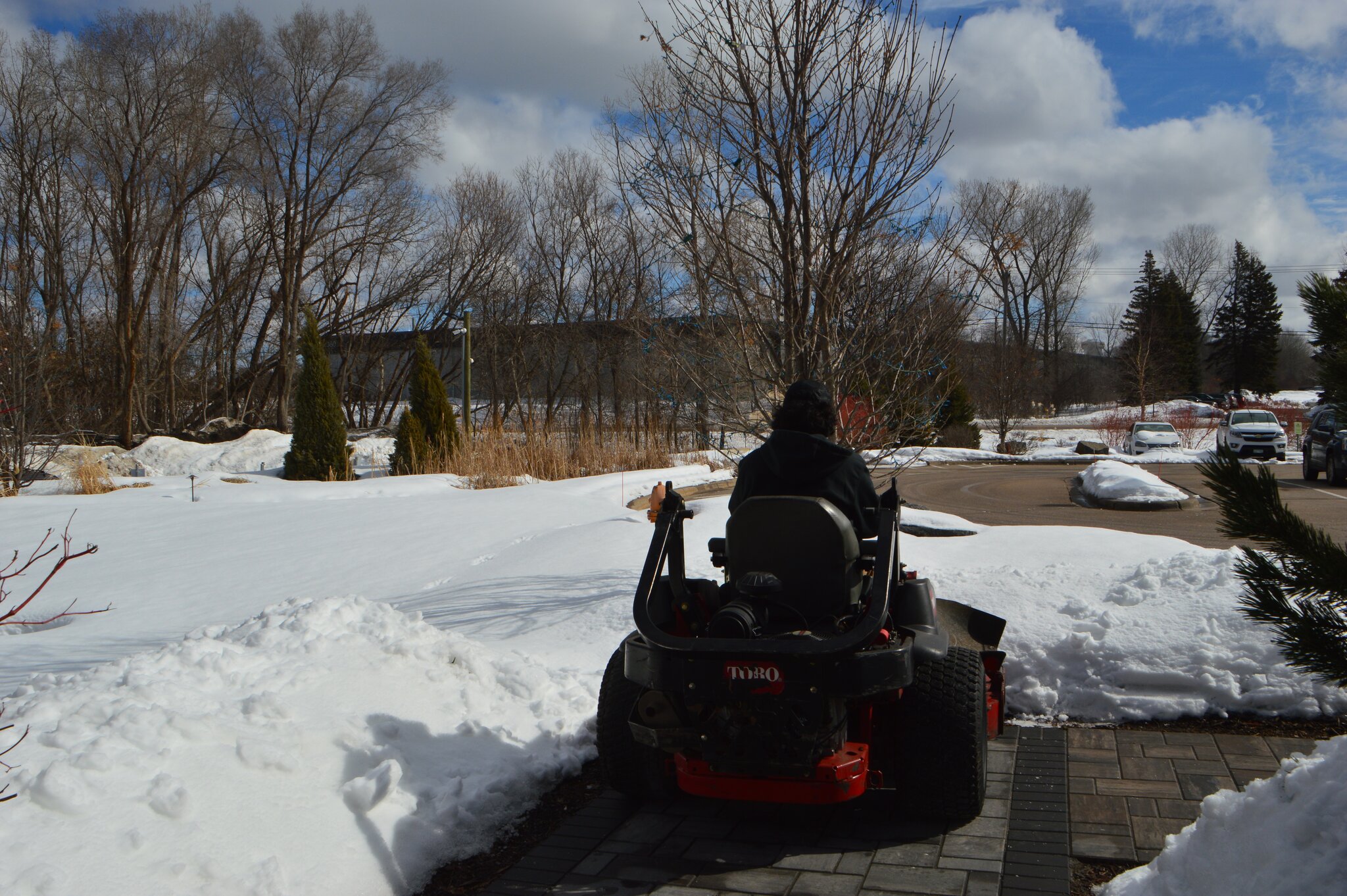 Person on lawn mower in snowy landscape.