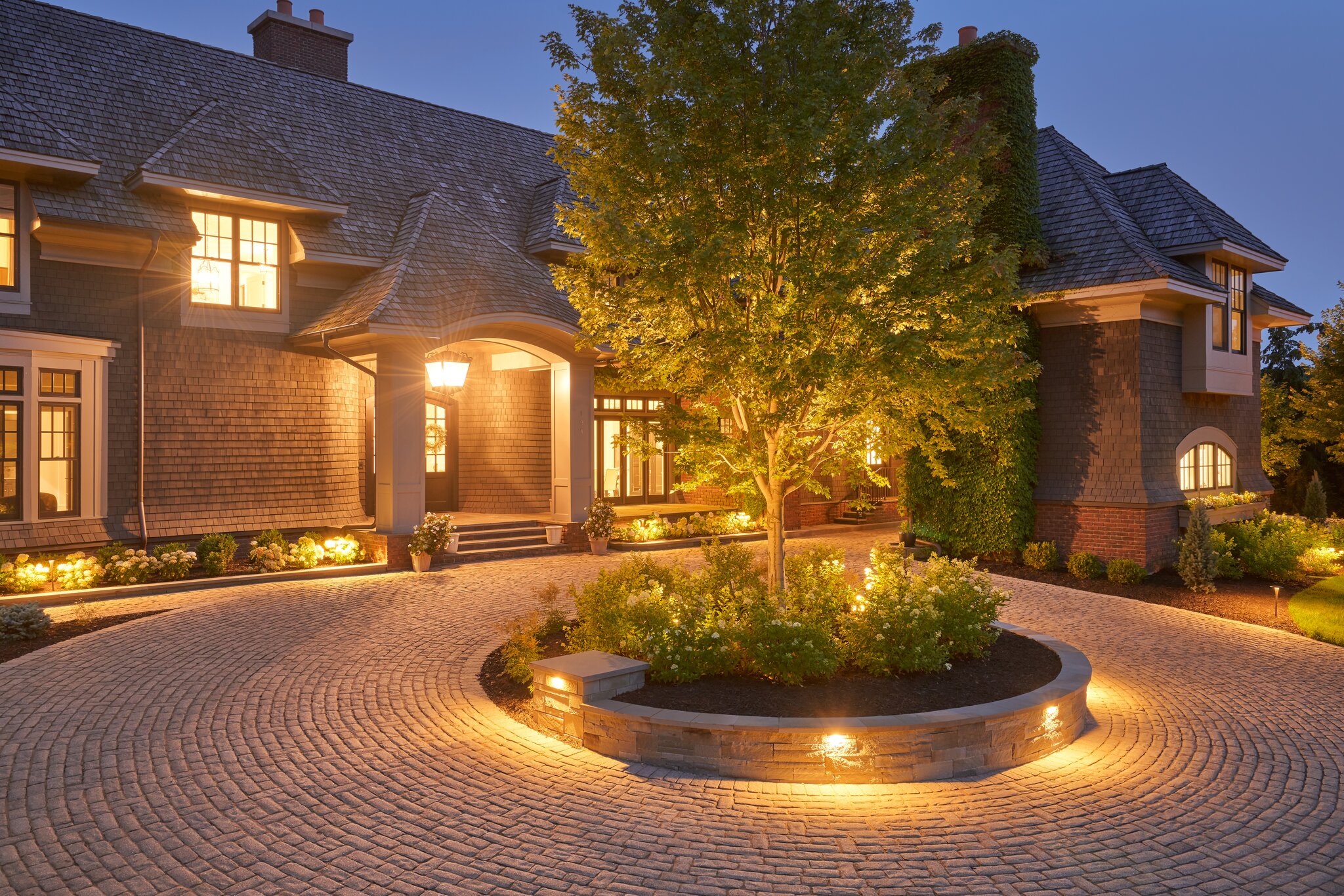 Elegant house with illuminated driveway and gardens.