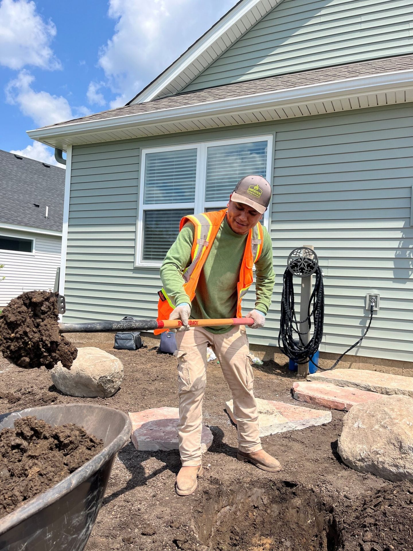 Worker shoveling soil in residential backyard landscaping.