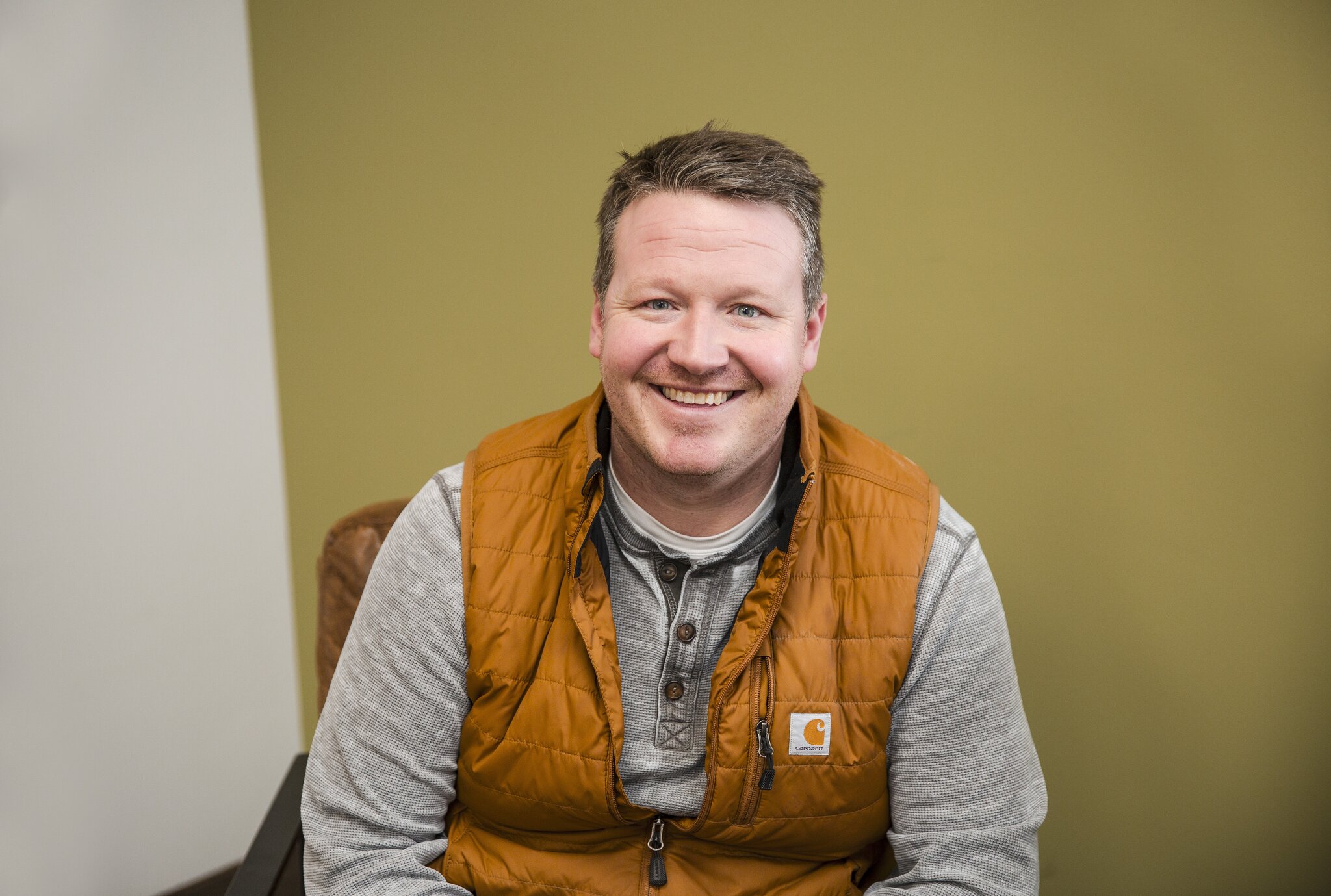 Smiling man in orange vest indoors.