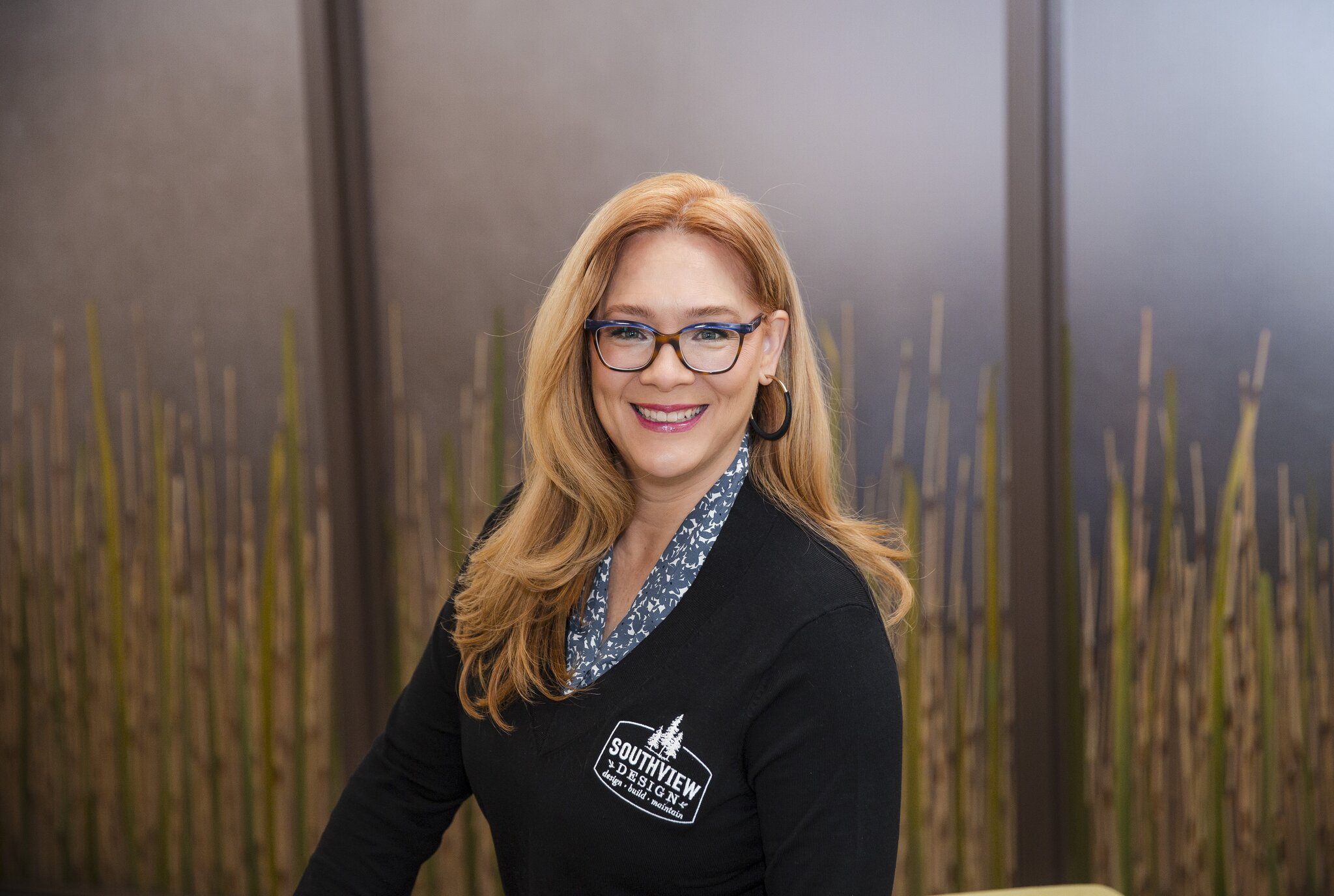 Smiling woman in front of decorative bamboo wall.