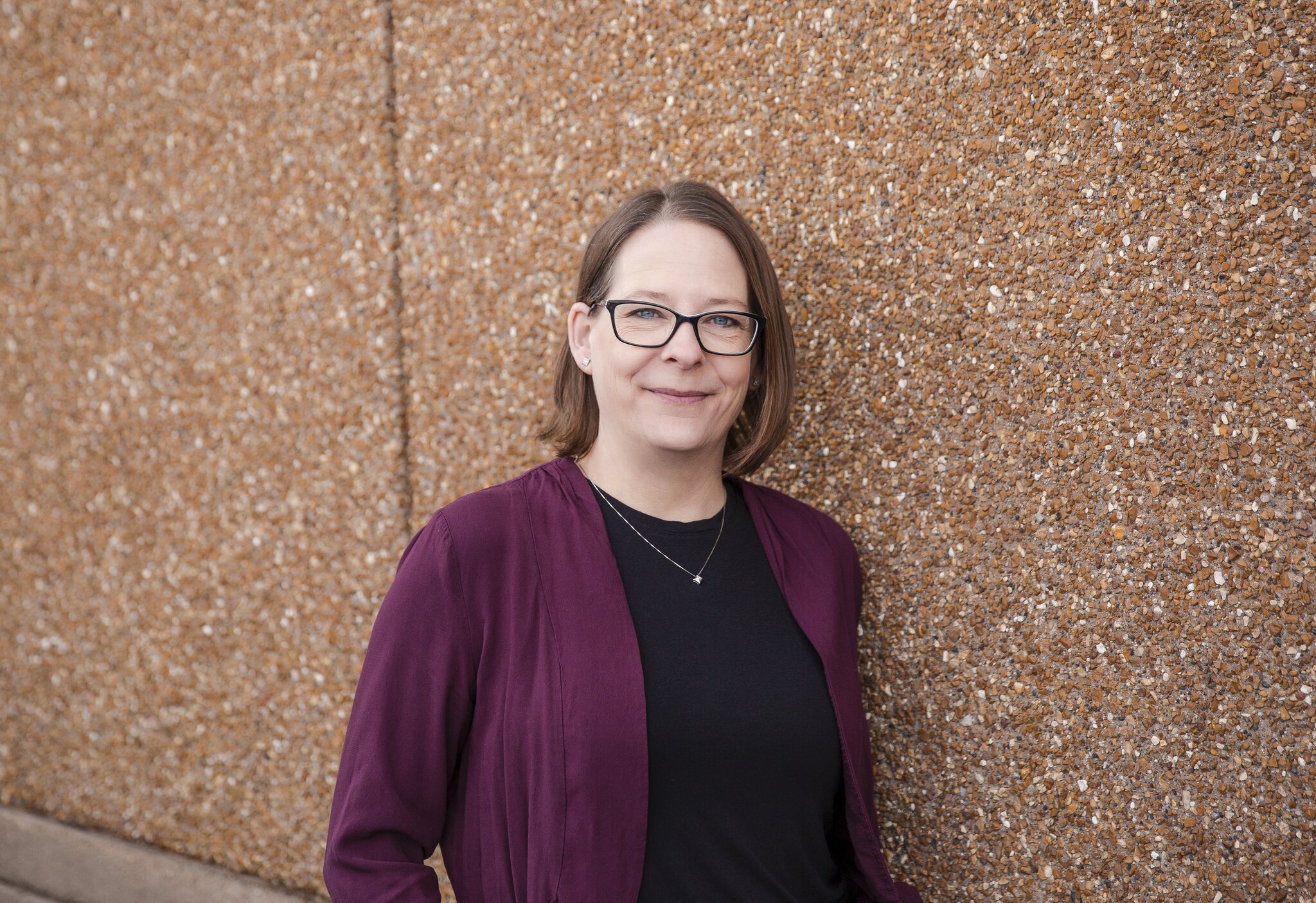 Person with glasses standing by textured wall.