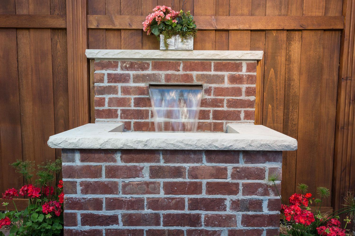 Brick garden fountain with flowers and wood fence