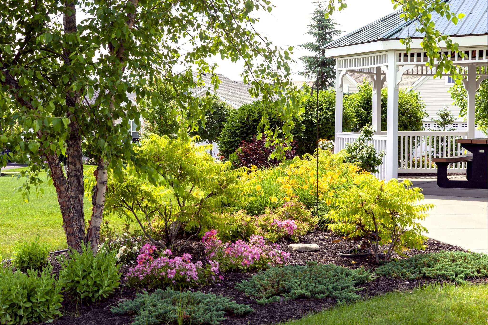 Garden with colorful flowers and white gazebo.