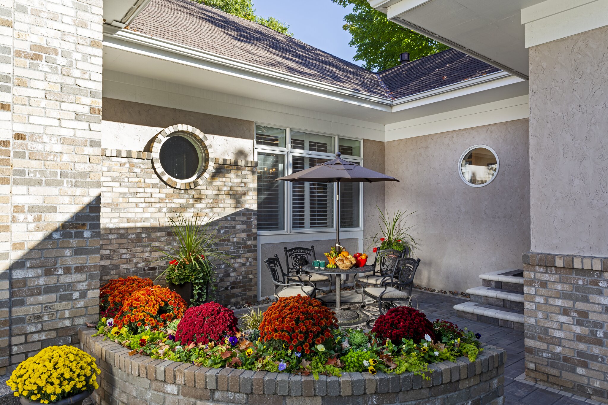 Patio with flowers, table, umbrella, and chairs.