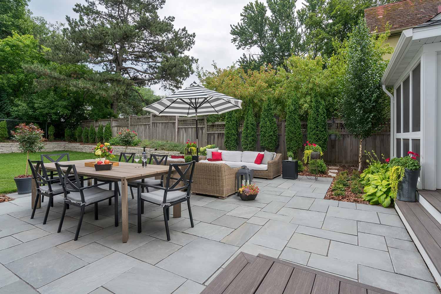 Backyard patio with furniture, umbrella, and greenery.