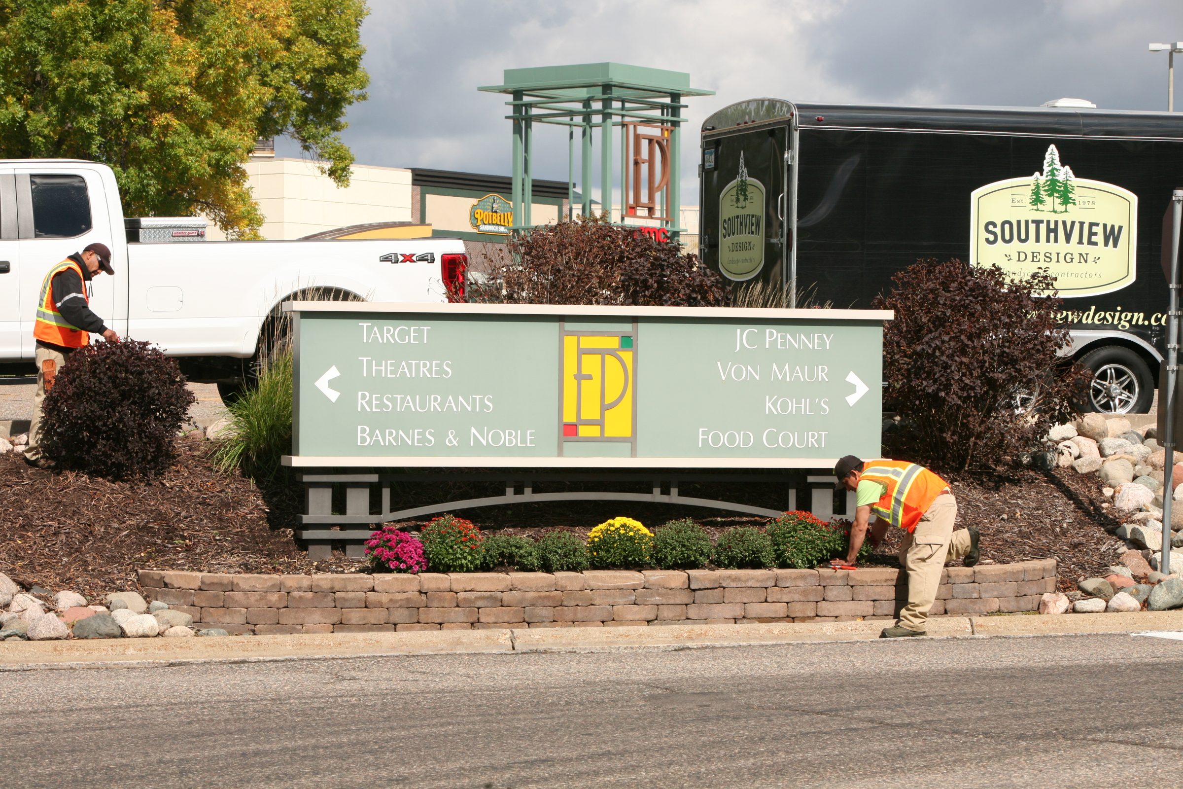 Shopping center sign with landscaping workers.
