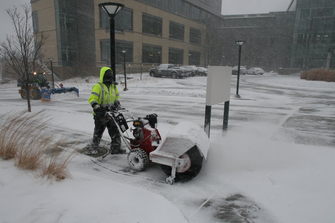 Worker clearing snow with snow blower outside building
