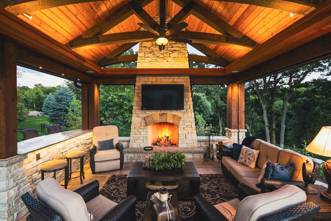 A four-season outdoor living room featuring a stone fireplace, warm wood accents, and comfortable seating — a hallmark of Minnesota outdoor living.