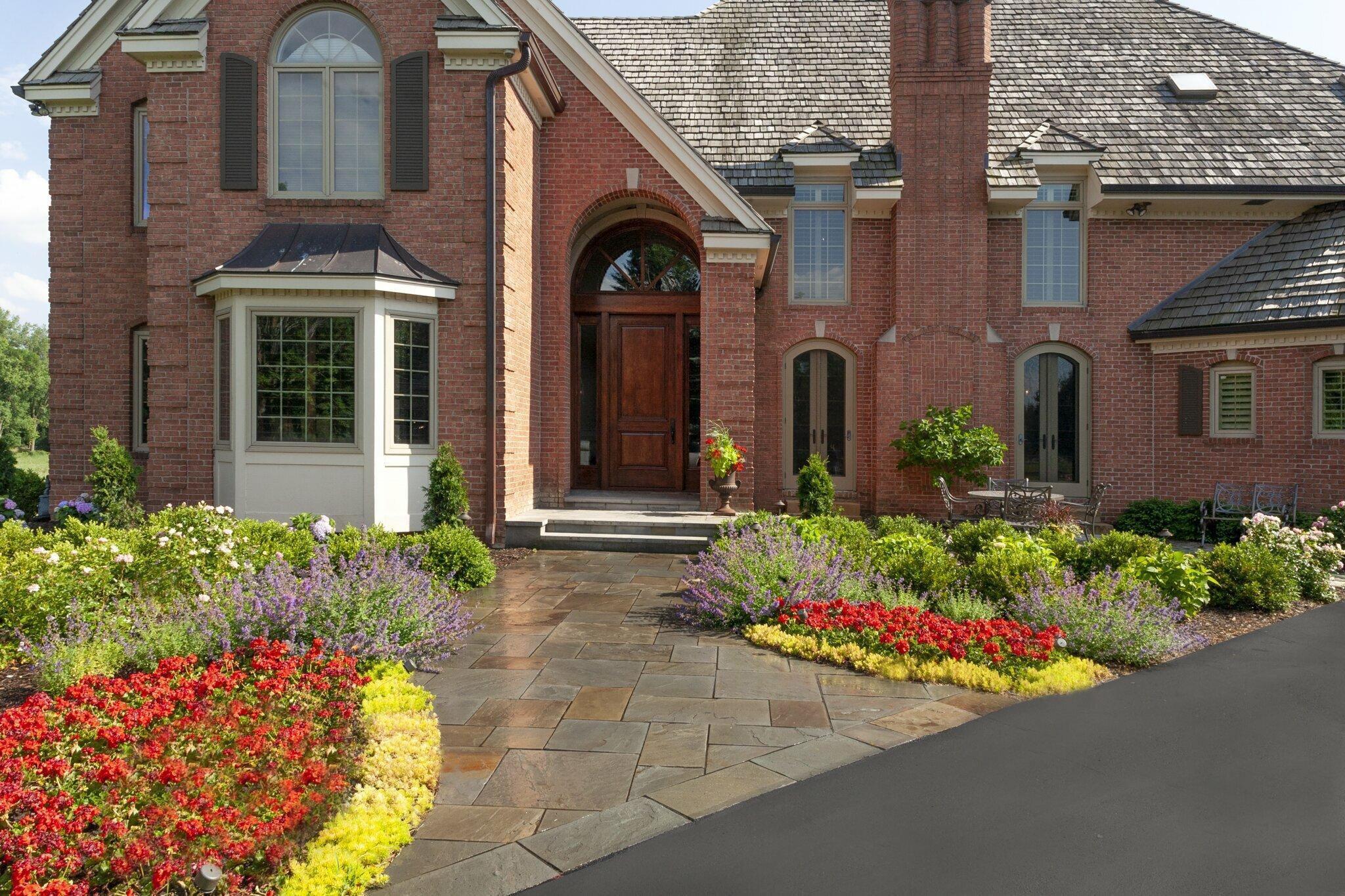 A welcoming front entry framed with bold color, layered perennials, and a natural stone walkway — showcasing curb appeal with year-round impact.