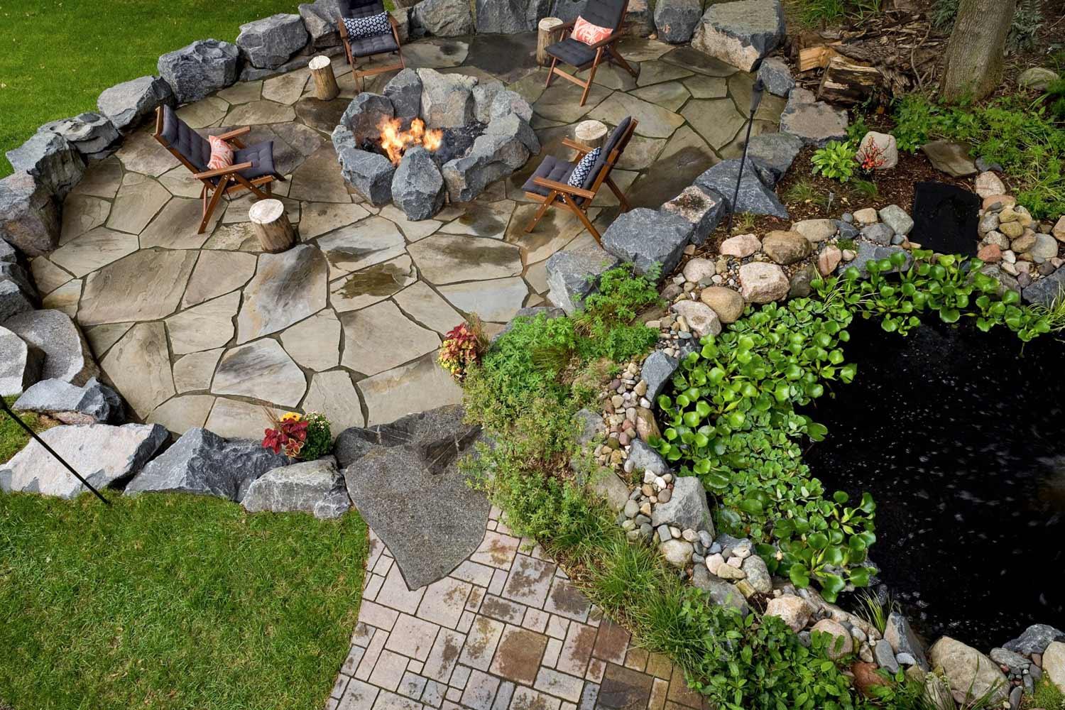 Backyard stone patio with fire pit and pond.